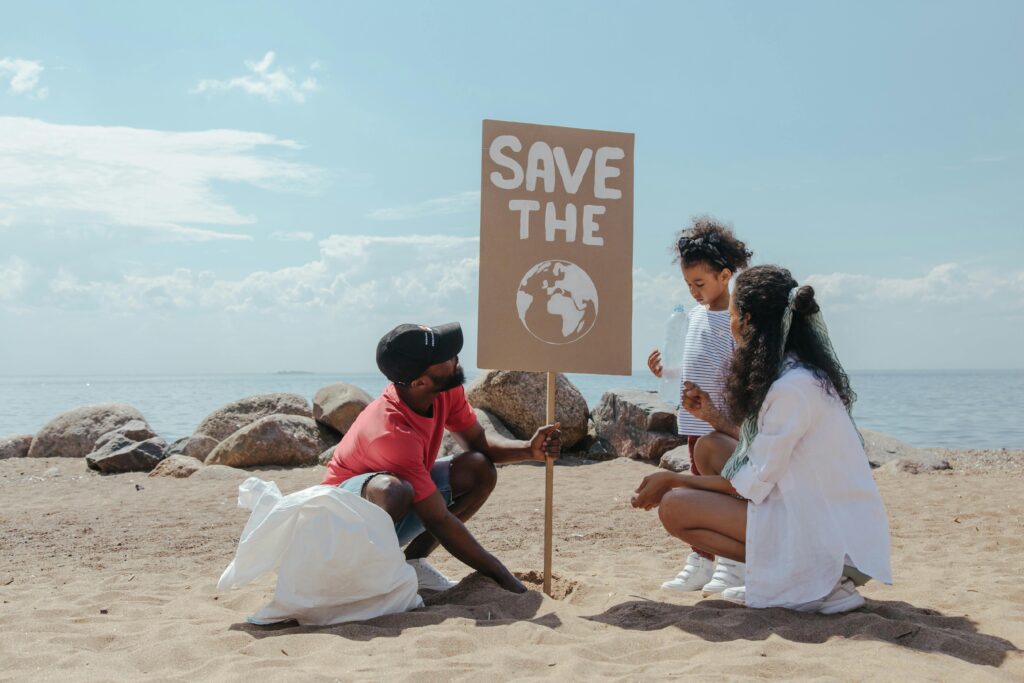 Family cleans beach, promoting environmental awareness with 'Save the Planet' sign.